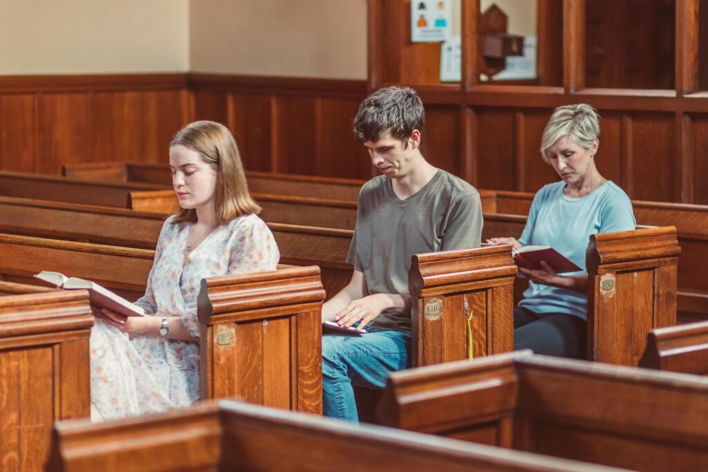 A man and two women reading inside a wooden church pew, focusing on scriptures.